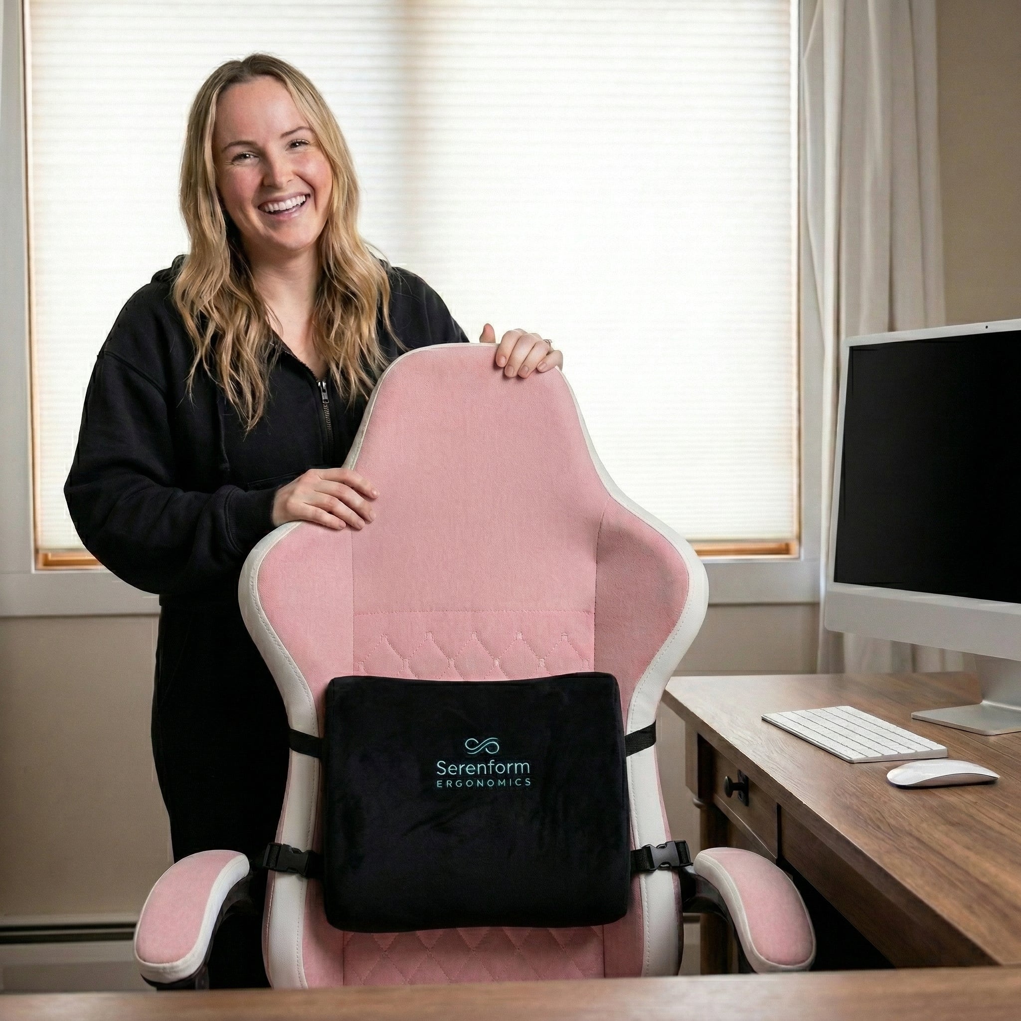 Woman holding a pink office chair with black Serenform lumbar pillow in a home office setting