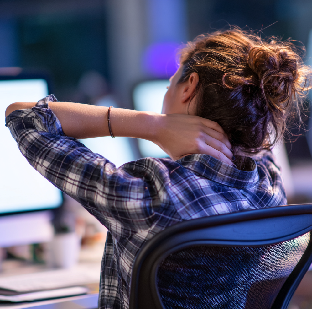 A desk worker sitting with poor posture—head forward and shoulders slouched—experiencing neck discomfort while working on a computer.