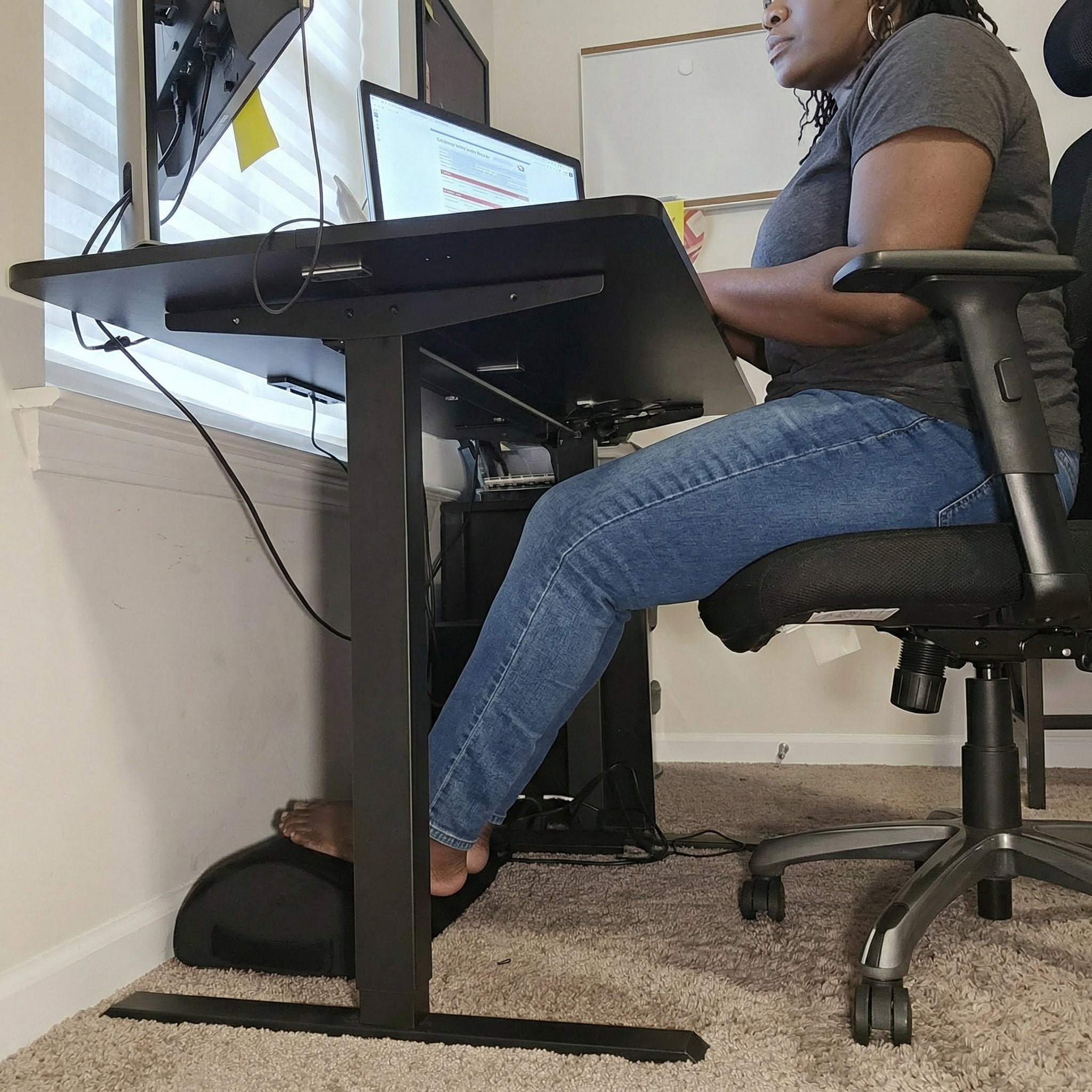 Person using footrest while sitting at a standing desk with multiple computer monitors in a home office