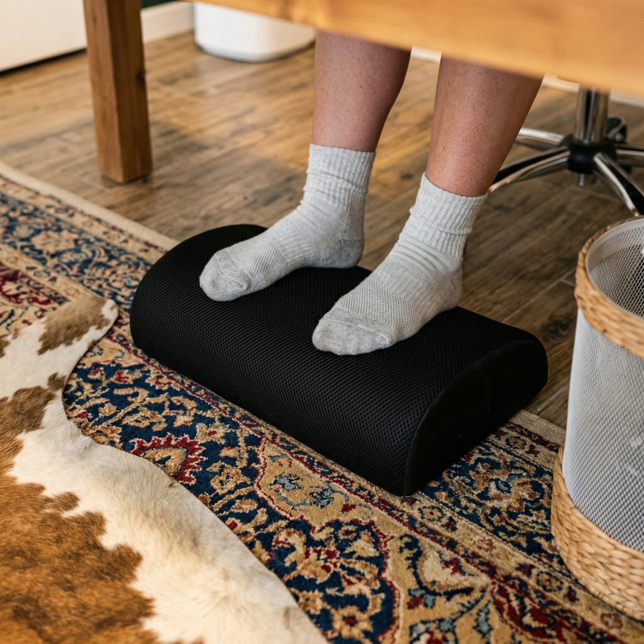Person using a footrest on a patterned rug in a home setting